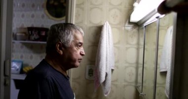 Sıradan yaşlı bir adam banyo aynasında kendine bakıyor.