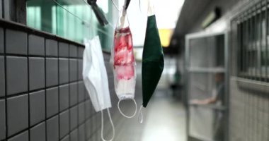 Yüz maskeleri dışarıda sallanıyor, kuruyor, arka planda yürüyen biri var.