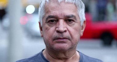 Pensive senior man standing outside staring camera. Middle-aged person portrait in city
