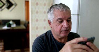 Older man checking cellphone at home, senior putting reading glasses on