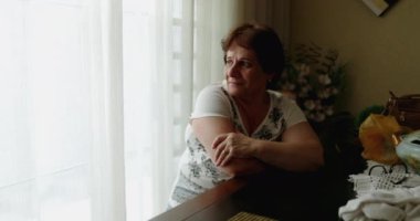 Evde pencereden bakan yaşlı bir kadın.