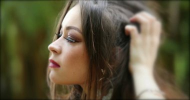 Yirmili yaşlarda, açık hava parkında poz veren, saçları düzelten kendinden emin genç bir kadın.