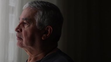 Contemplative senior standing by window curtains