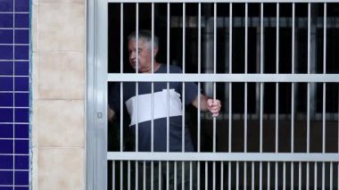 Older man opening metal gate manually and observing neighborhood