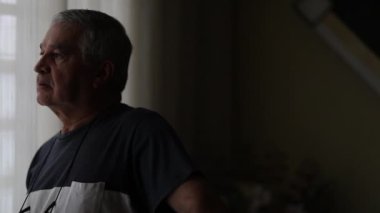 Pensive older man standing by window