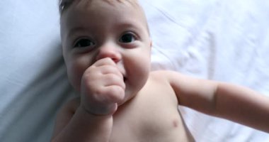 Sevimli bebek kameraya yapışıyor, tatlı bebek yatakta yatıyor.