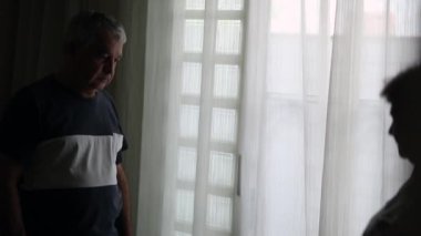 Depressed older couple by window looking down in shadows