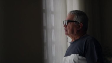 Preoccupied senior man standing by window waiting anxiously