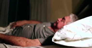 Senior man turning bedside lamp on in the middle of the night suffering from insomnia