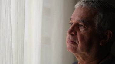 Pensive older man standing by window looking out