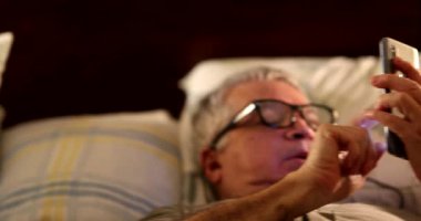 Married older couple in bed using cellphone device, addicted people on social media