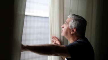 Suspicious older man spying outside through window blinds