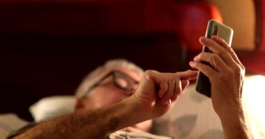 Evli çift yatakta akıllı telefon kullanıyor.