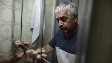 Depressed older man suffering in front of bathroom mirror