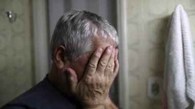 Troubled senior man looking at bathroom mirror suffering mental illness