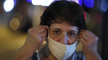 Senior woman putting covid-19 face mask at night in city
