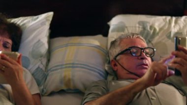 Older couple in bed using cellphone. Middle aged husband and wife sharing screens at night before sleep