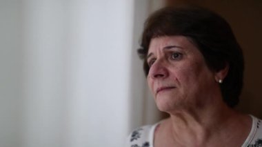 Older woman standing by window looking outside observing