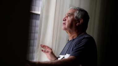Elder man standing by window looking out surveilling noise