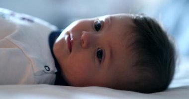 Sevimli bebek yatakta uzanmış, kamera portresine bakıyor.