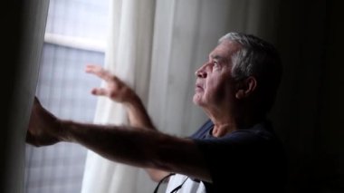 Older man peeking out outside survelling neighbors. Curious Senior person standing by window observing