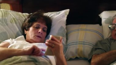 Married older couple in bed using smartphone before sleep