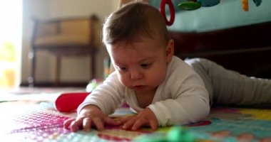 Bebek yerde uzanmış oyun hasırına dokunuyor, bebek dünyayı keşfediyor.