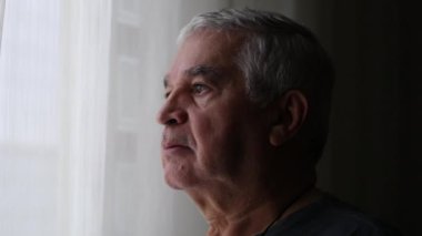 Pensive older man standing by window looking out