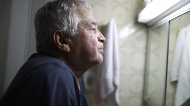 Созерцательный Пожилой Мужчина Страдает Одиночестве Перед Зеркалом Ванной Комнаты — стоковое видео