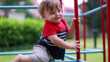 Joyful baby boy playing at playground climbing on monkey bar