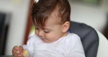 Bebek evde sandalyede muz yiyor.