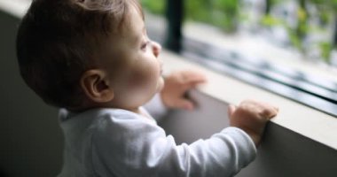 Ev penceresinin yanında durup dışarıyı seyreden sevimli bir bebek. Çocuk çocuk dışarı bakıyor.