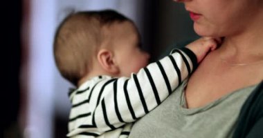Mother holding baby infant in arm. Toddler reaching for mom necklace