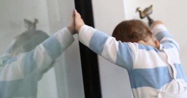 Evdeki pencereye yaslanmış şirin bir bebek gelişimi. Çocuk ayağa kalktı.