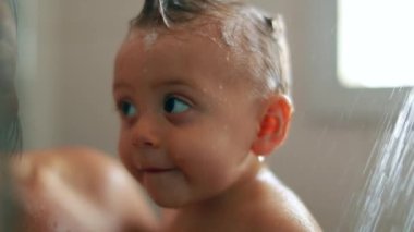 Cute baby inside shower with mother. Infant toddler looking to camera while bathing