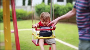Baby at playground swing, grand-father pushing toddler infant at swing