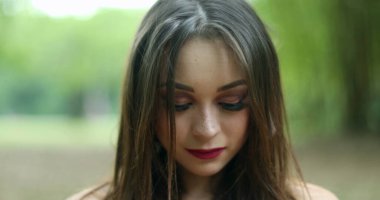 20 'li yaşlarda derin bir nefes alan bir kız. Parkta temiz hava soluyan genç bir kadın kameraya bakıyor kendini yenilenmiş ve mutlu hissediyor.