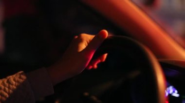 Hand holding steering wheel at night waiting in traffic at red light