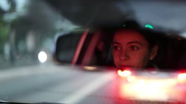 Woman driver seen from rear view mirror in traffic at night