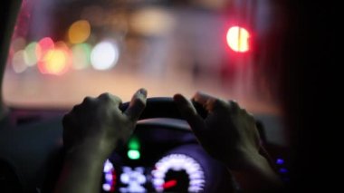Hands holding steering wheel waiting in red light traffic at night
