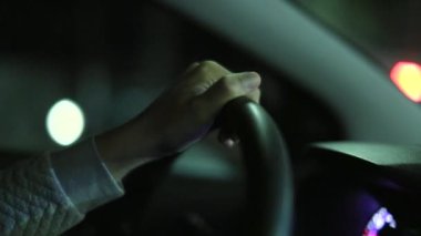 Female hands holding steering wheel driving at night in city