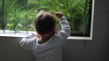 Adorable baby standing by home window looking outside