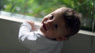Smiling baby portrait turning head to camera. One year old toddler infant smiles portrait by window