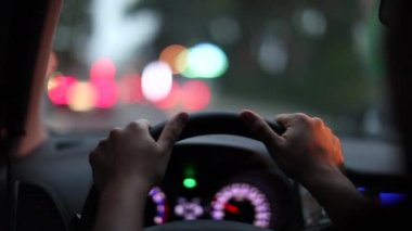 Close-up hands holding steering wheel driving in city at night