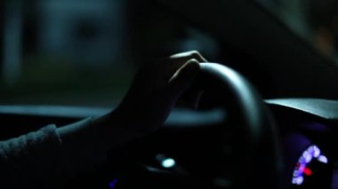 Hand close-up holding steering wheel driving in urban city in dark