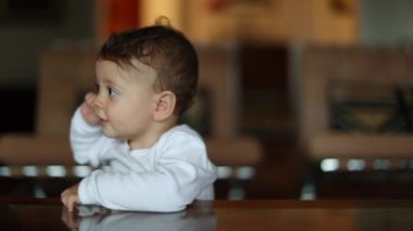 Cute one year old baby at home leaning by table. Toddler infant standing at home portrait