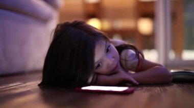 Little girl lying on floor at home at night grabbing cellphone device