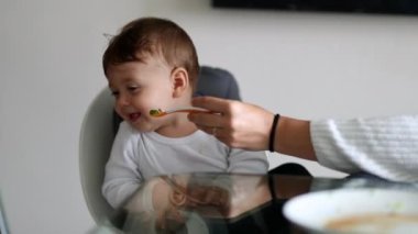 Baby rejecting food, mother trying to feed one year old infant toddler