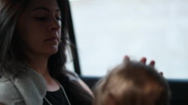 Mother and baby child in back seat of car, mom looking out car window, infant toddler playing with necklace