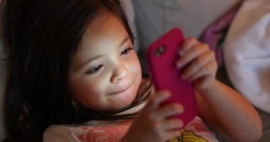 Child using smartphone device at night. Little girl holding cellphone in evening